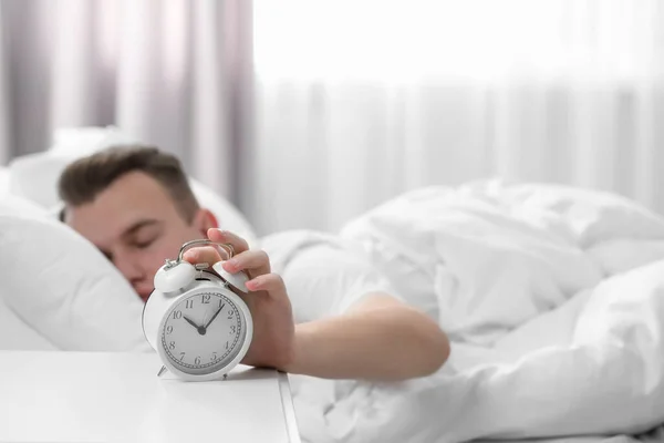 Sleepy man turning off alarm clock at home in morning, focus on hand. Space for text