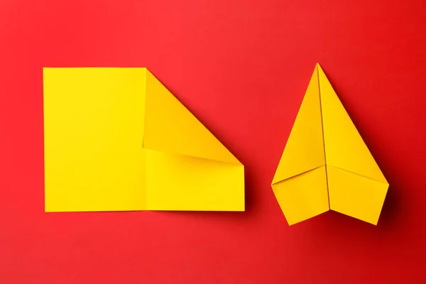 Handmade yellow plane and folded piece of paper on red background, flat lay