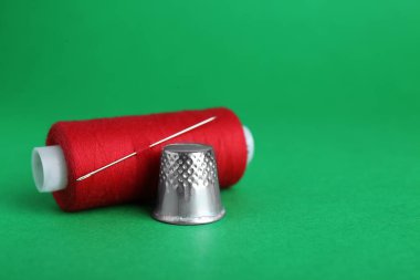 Silver thimble, thread and needle on green background, space for text. Sewing accessories