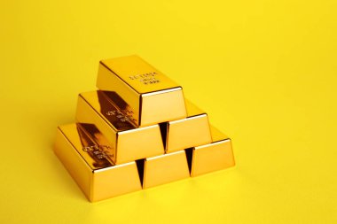 Stack of shiny gold bars on yellow background