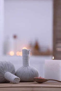 Spa composition with burning candle and herbal bags on massage table in wellness center, space for text