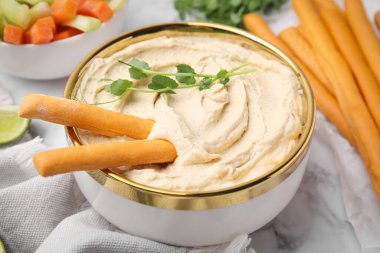 Delicious hummus with grissini sticks served on white marble table, closeup