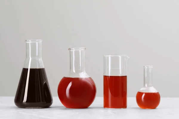 Different laboratory glassware with brown liquids on white table against light background