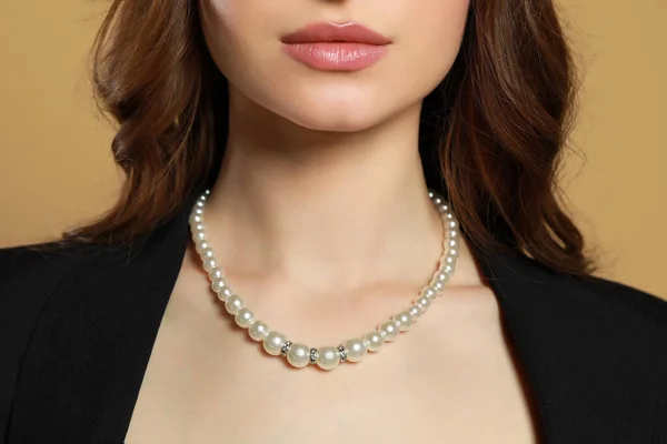 Young woman with elegant pearl necklace on brown background, closeup