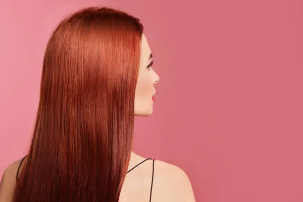 Beautiful woman with red dyed hair on pink background, back view. Space for text