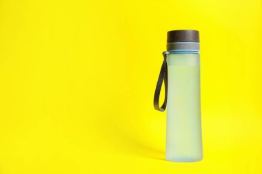 Stylish closed bottle with water drops on yellow background, space for text