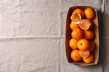 Paper box with fresh ripe tangerines on beige cloth, top view. Space for text