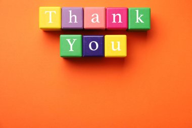 Colorful cubes with phrase Thank You on orange background, top view