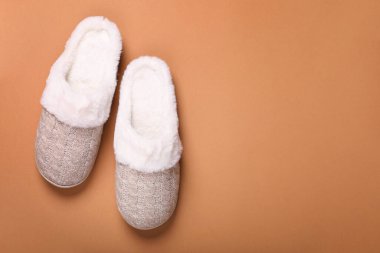 Pair of beautiful soft slippers on light brown background, top view. Space for text
