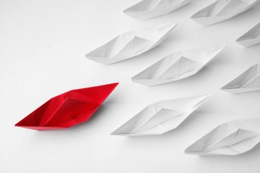 Group of paper boats following red one on white background, flat lay. Leadership concept