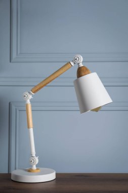 Stylish modern desk lamp on wooden table near light grey wall