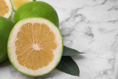 Whole and cut sweetie fruits with green leaves on white marble table, closeup. Space for text