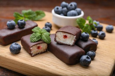 Delicious glazed curd snacks with blueberries on wooden table, closeup clipart