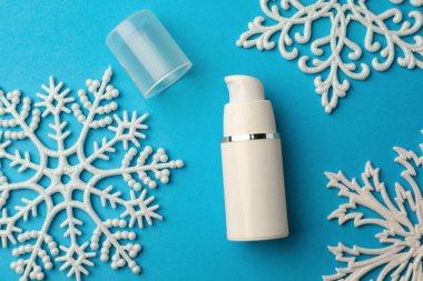 Hand cream and snowflakes on light blue background, flat lay. Winter skin care