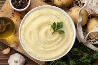 Bowl of tasty mashed potato, parsley, garlic, olive oil and pepper on wooden table, flat lay
