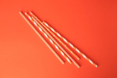Striped paper drinking straws on orange background, flat lay