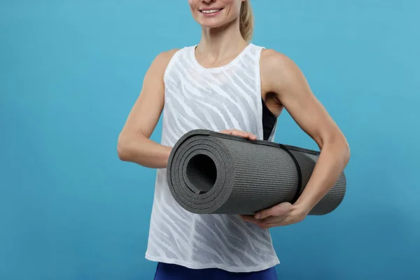 Sportswoman with fitness mat on light blue background, closeup