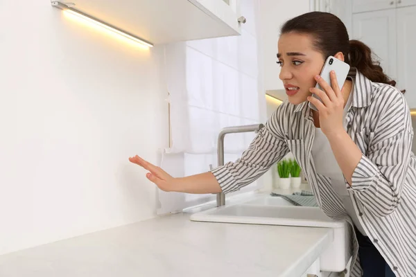Confused woman talking on phone and looking at wall in kitchen