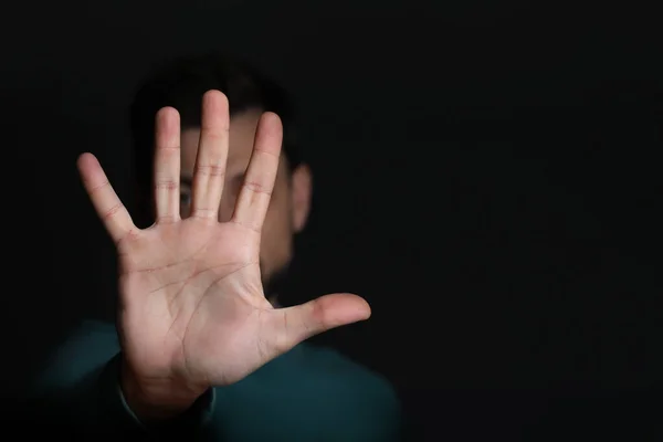 Man showing stop gesture against black background, focus on hand. Space for text