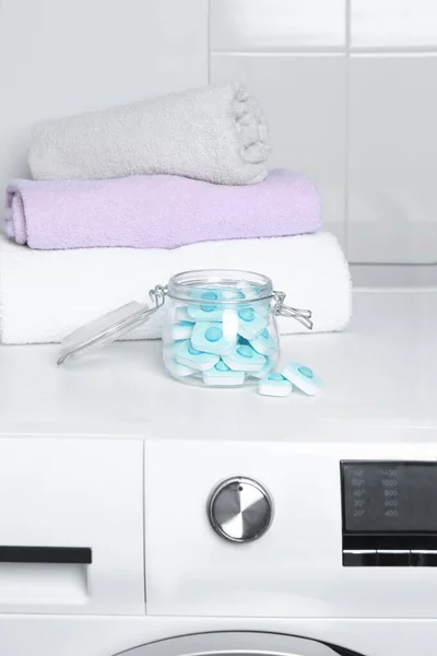 Jar with water softener tablets near stacked towels on washing machine