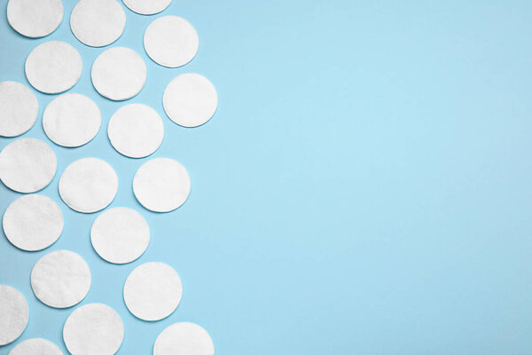 Many cotton pads on light blue background, flat lay. Space for text