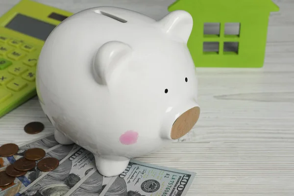 Piggy bank, house model, calculator and money on white wooden table, closeup. Space for text