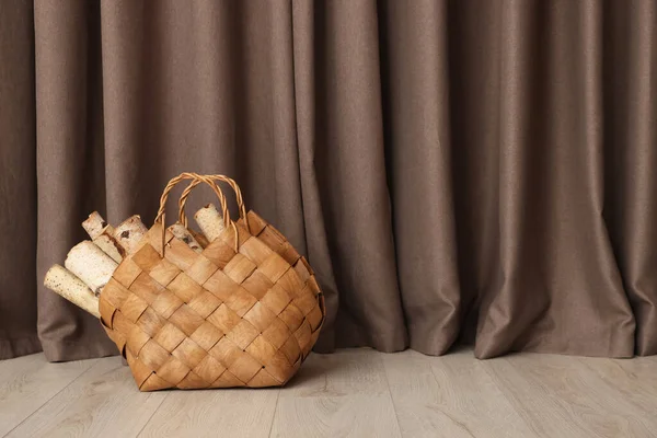 Wicker bag with firewood on floor near elegant curtains indoors, space for text