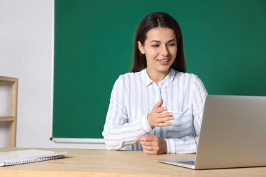 Genç öğretmen sınıfta masada ders veriyor.