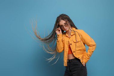 Beautiful woman with long african braids and sunglasses on blue background, space for text