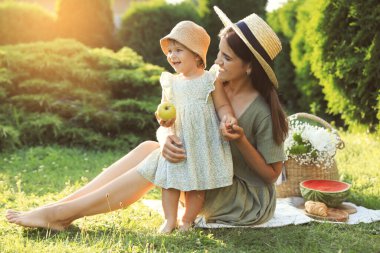 Mother with her baby daughter having picnic in garden on sunny day
