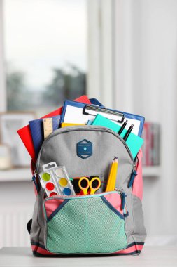 Backpack with different school stationery on white table indoors