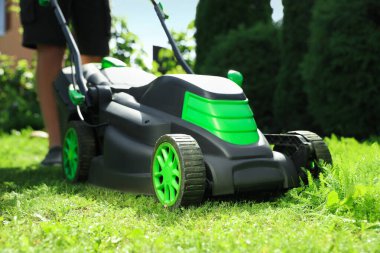 Güneşli bir günde bahçede çim biçme makinesiyle çim biçen adam, yakın plan.