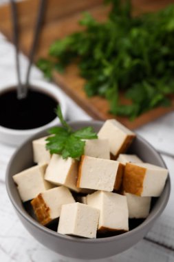 Tütsülenmiş tofu küpleri, soya sosu ve maydanoz beyaz ahşap masa, yakın plan.
