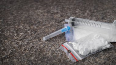 Plastic bag with powder, syringe and pills on stone surface, space for text. Hard drugs
