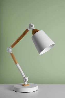 Stylish modern desk lamp on white table near light green wall