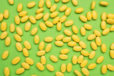 Many yellow dragee candies on green background, flat lay