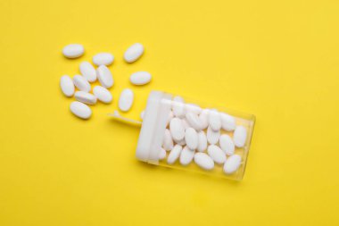 Tasty dragee candies and container on yellow background, flat lay