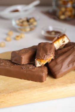 Board with delicious chocolate bars and nuts on white wooden table, closeup