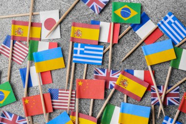 Many small paper flags of different countries on grey table, flat lay
