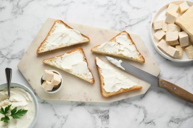 Delicious toasts with tofu cream cheese and parsley on white marble table, flat lay.