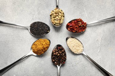 Metal spoons with different spices on light grey table, flat lay