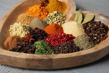 Heart shaped plate with different spices on grey wooden table, closeup
