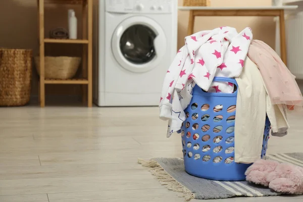 Laundry basket with baby clothes and fluffy slippers on wooden floor in bathroom, space for text