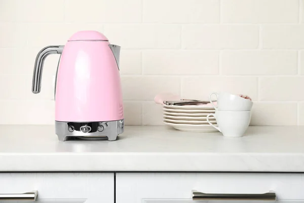 Modern electric kettle and dishes on counter in kitchen