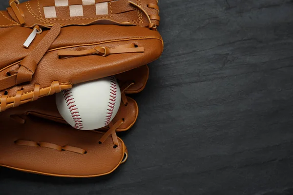 Catcher\'s mitt and baseball ball on black slate background, top view with space for text. Sports game