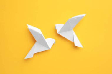 Origami art. Colorful handmade paper birds on yellow background, flat lay
