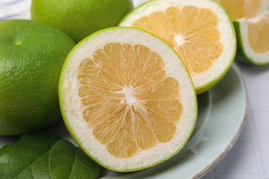 Whole and cut sweetie fruits with green leaves on white tiled table, closeup
