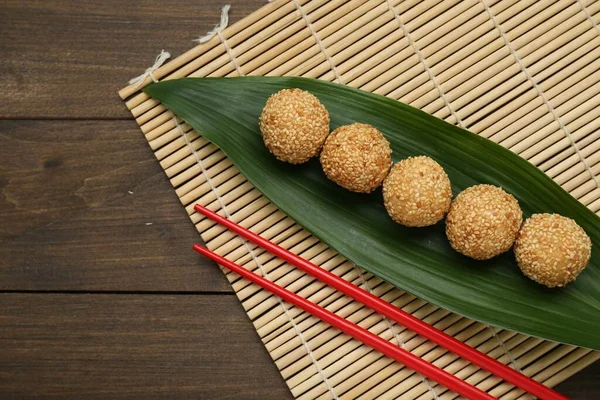 Delicious sesame balls, green banana leaf and chopsticks on wooden table, flat lay. Space for text