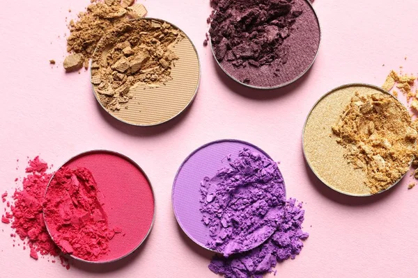 Different crushed eye shadows on pink background, flat lay