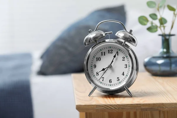 Silver alarm clock on wooden nightstand in bedroom, space for text